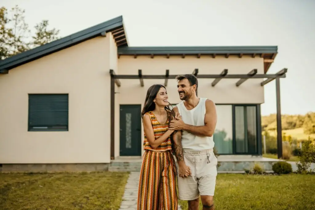 Couple standing outside a single story home with a pergola
