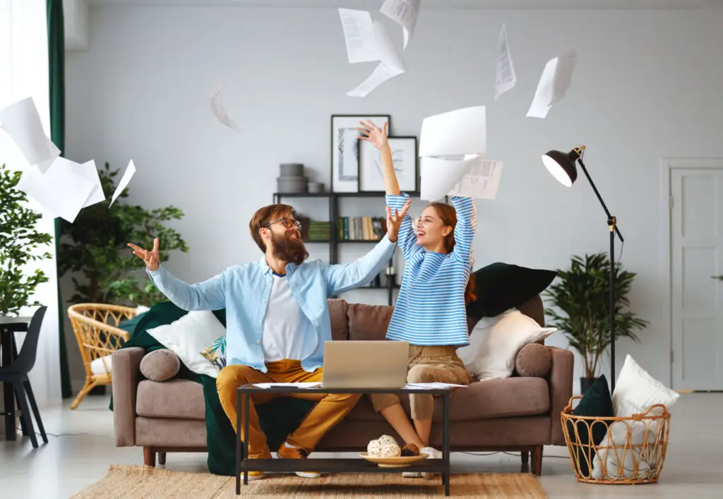 Couple celebrating at home as papers fly above their laptop