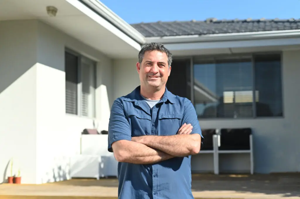 Self employed homeowner standing with his arms crossed outside his home